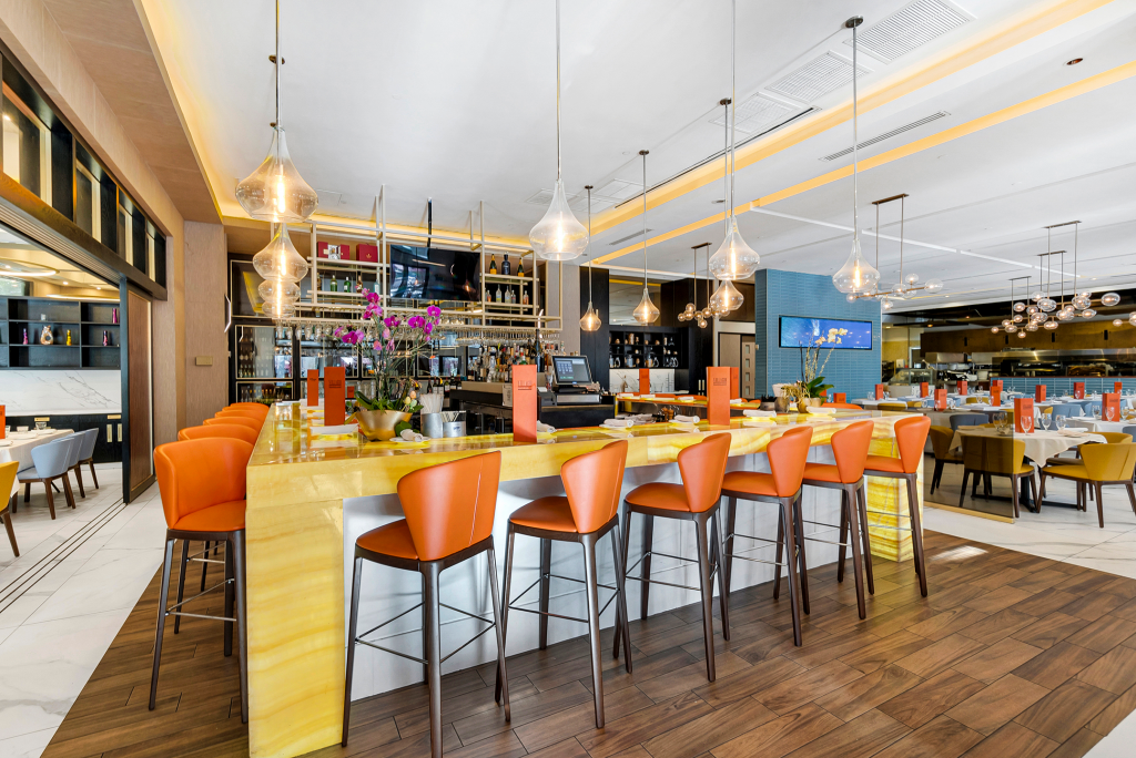 Large yellow Onyx bar with orange bar stools that surround. Over all view of restaurant.