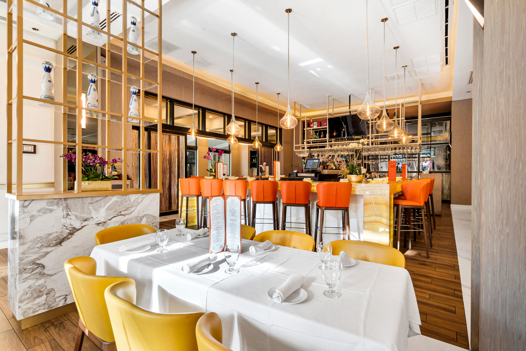 Dining table behind host stand with bar located diagonally.