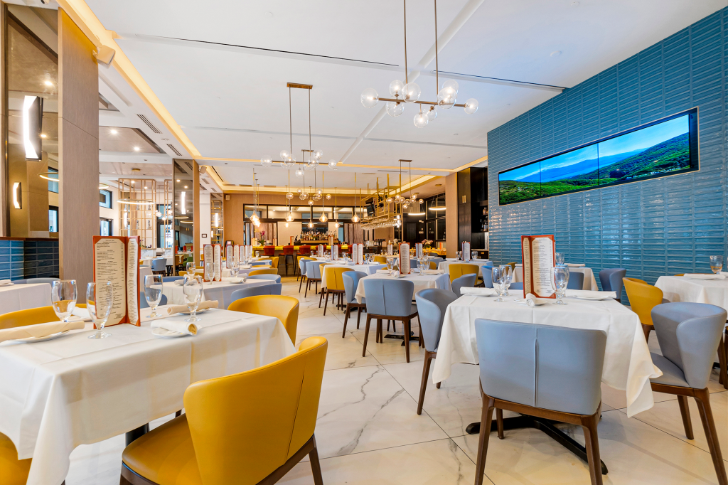 Opposite side of restaurant that over looks large sitting area. Blue thin tile wall with monitors in landscape format showing pictures of italy